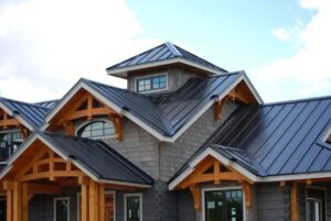 Modern house with grey shingles, metal roofs, and wooden accents under a blue sky.