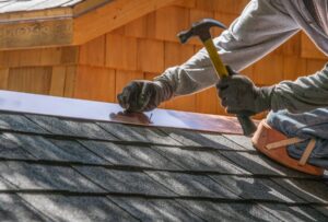 Worker hammering a nail on a roof with shingles on a sunny day.