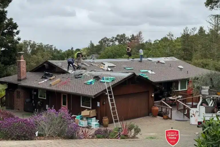 Two workers replace roof of wooden house with tools on roof and ladder leaning against the side
