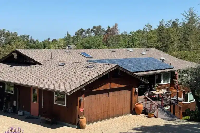 Modern wooden house with sloped roof, solar panels, trees, and patio with outdoor furniture