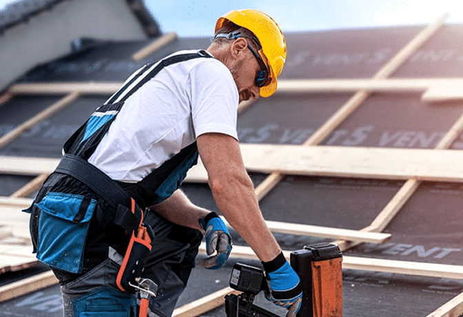 Roofer with power drill on residential roof under clear skies, showing expert, durable service.