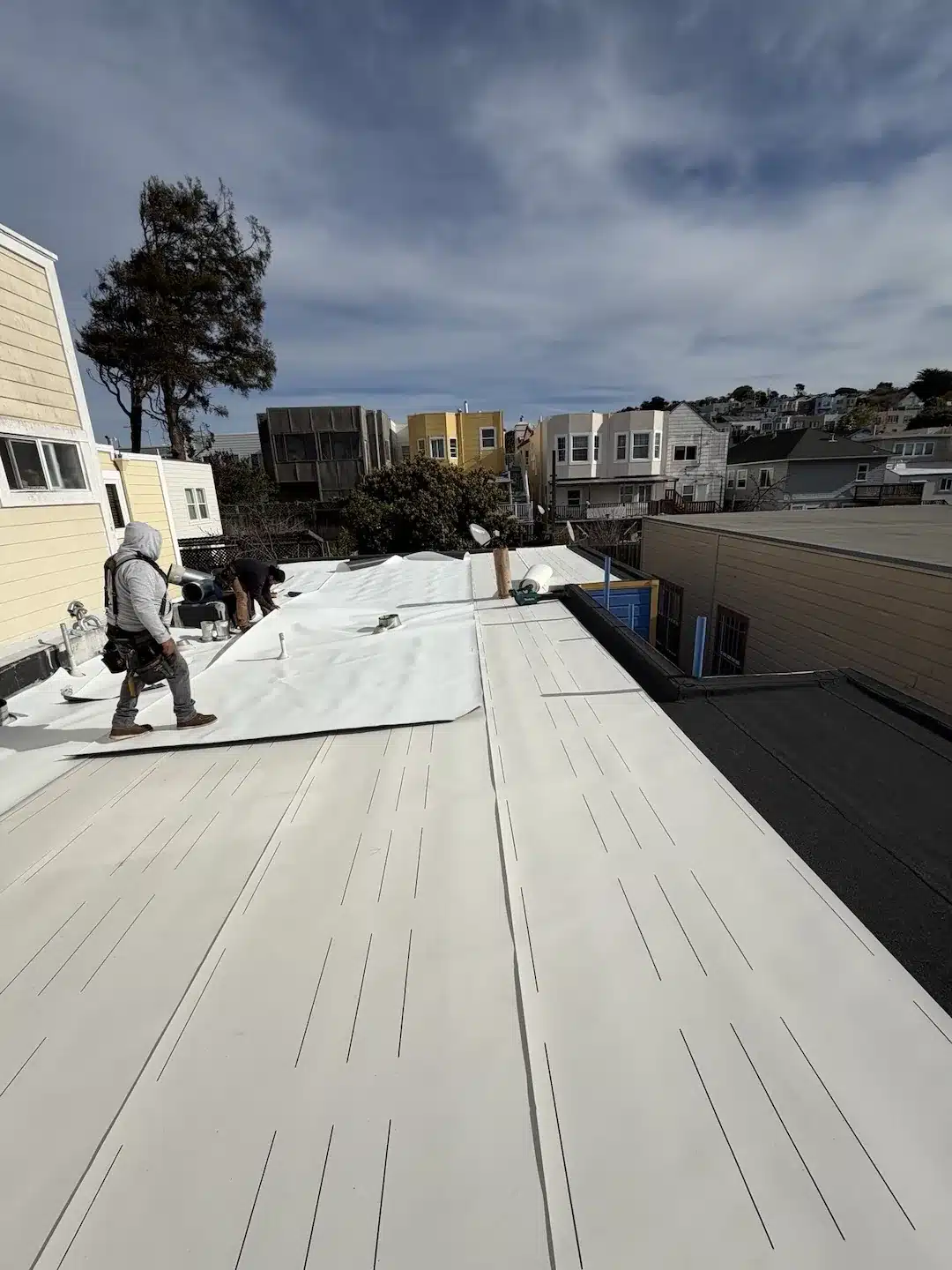 Crew rolling out white TPO membrane over the prepared flat roof at 1582 Quesada Ave San Francisco