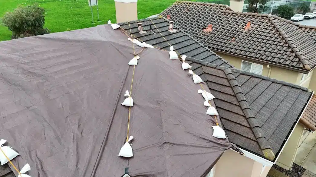 Tarps covering two sections of a concrete tile roof before underlayment replacement in South San Francisco