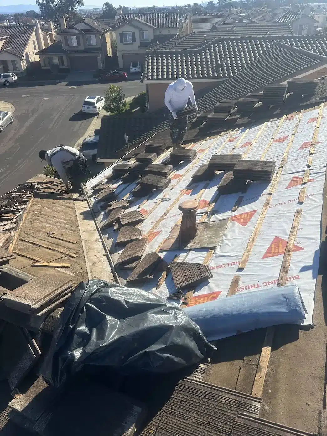 Crew lifting and stacking concrete tiles over new Sika synthetic underlayment during tile roof repair in South San Francisco
