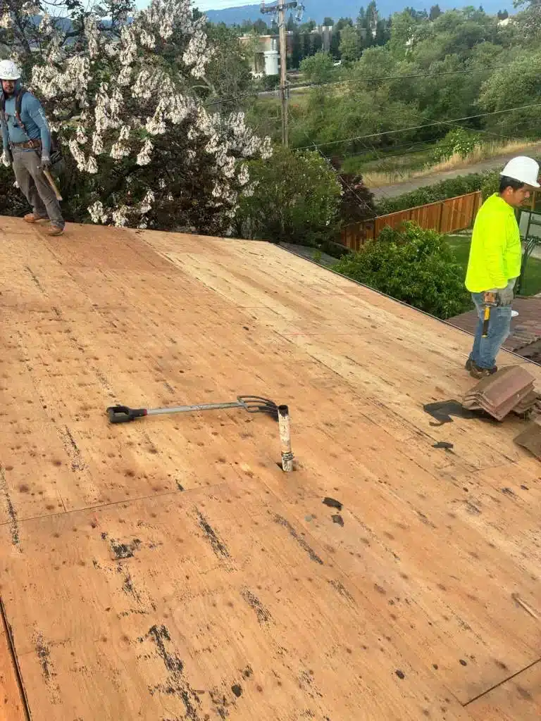 Lifetime Roofing & Renovation crew removing old concrete tile down to the plywood decking on a San Jose roof, with stripped tiles stacked to the side
