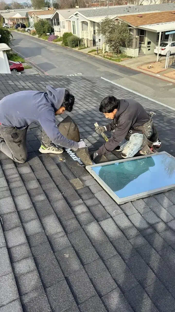 Roofers pulling back shingle courses around the skylight opening during replacement in Sunnyvale, CA