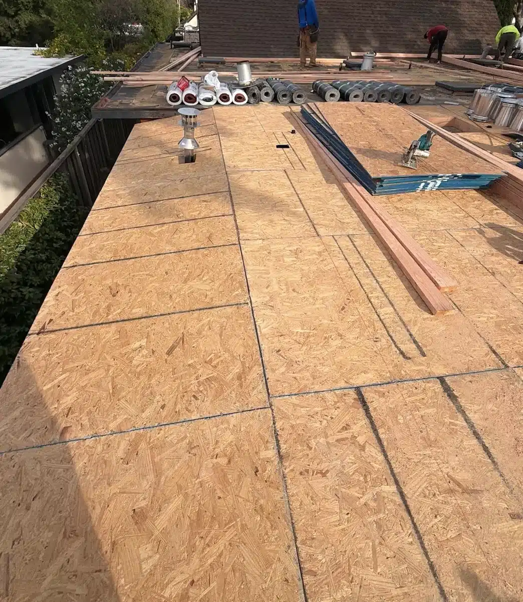 New structural sheathing installed across the flat roof with cap sheet rolls and vent flashings staged, Sunnyvale CA