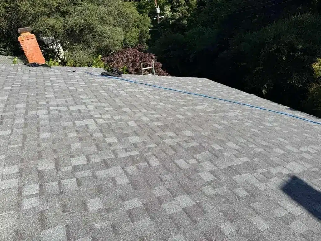 Finished architectural shingle roof beside the original brick chimney after a full tear-off