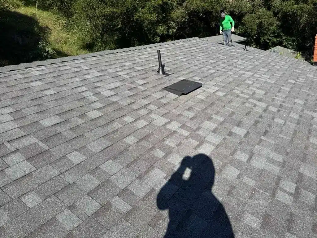 Roofer on the completed shingle roof beside a newly installed vent and pipe boot in the Oakland Hills