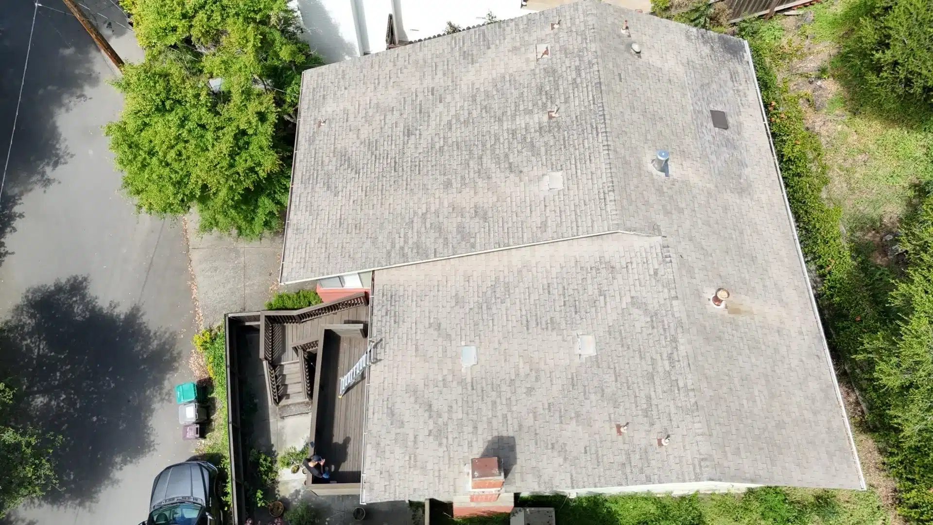 Overhead drone view of the worn shingle roof showing patchy discoloration across both roof planes