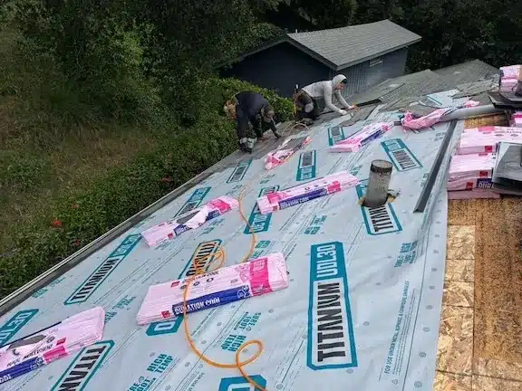 Roofing crew loading architectural shingle bundles onto synthetic underlayment and new sheathing