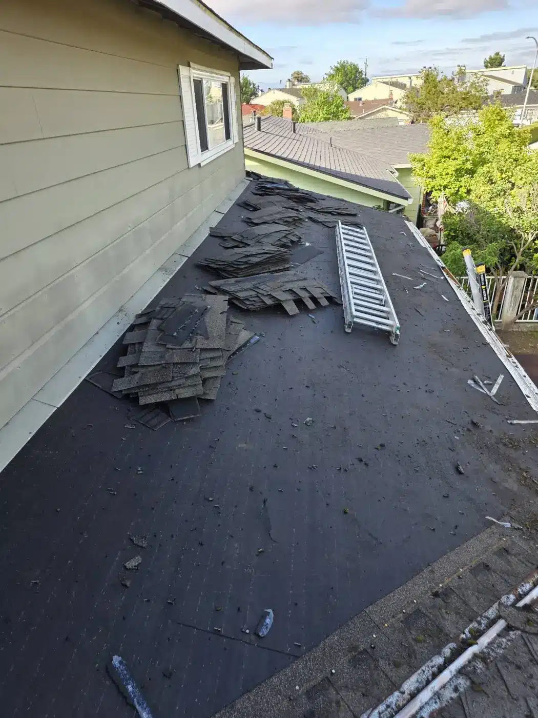Tear-off in progress with old shingles stacked on the exposed roof deck in Milpitas, CA