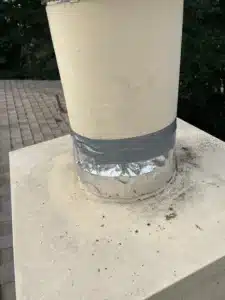Foil tape wrapped around the base of a metal flue where it meets the chimney chase crown on a Hayward roof, used in place of proper flashing