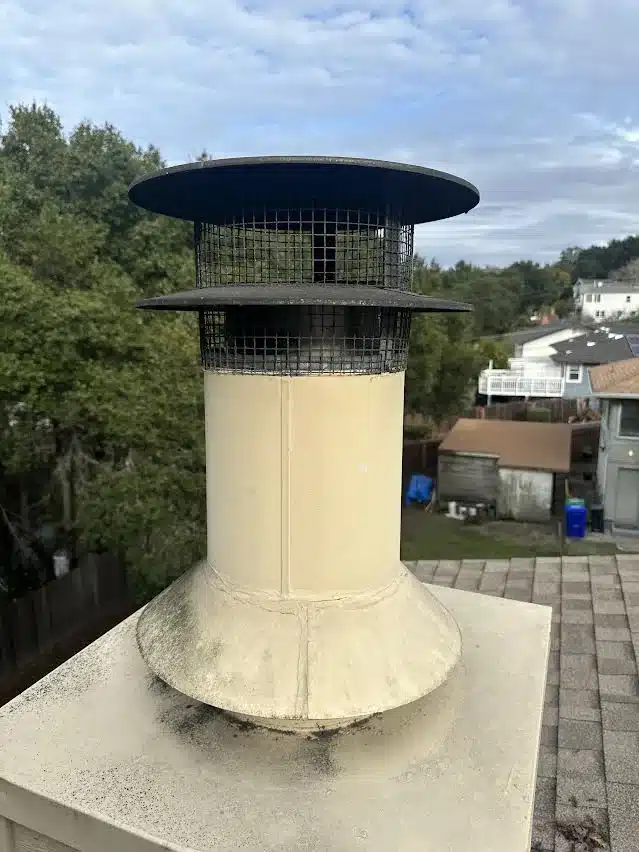 Metal flue and rain cap on a chimney chase in Hayward with a stained, weathered flashing collar at its base before repair