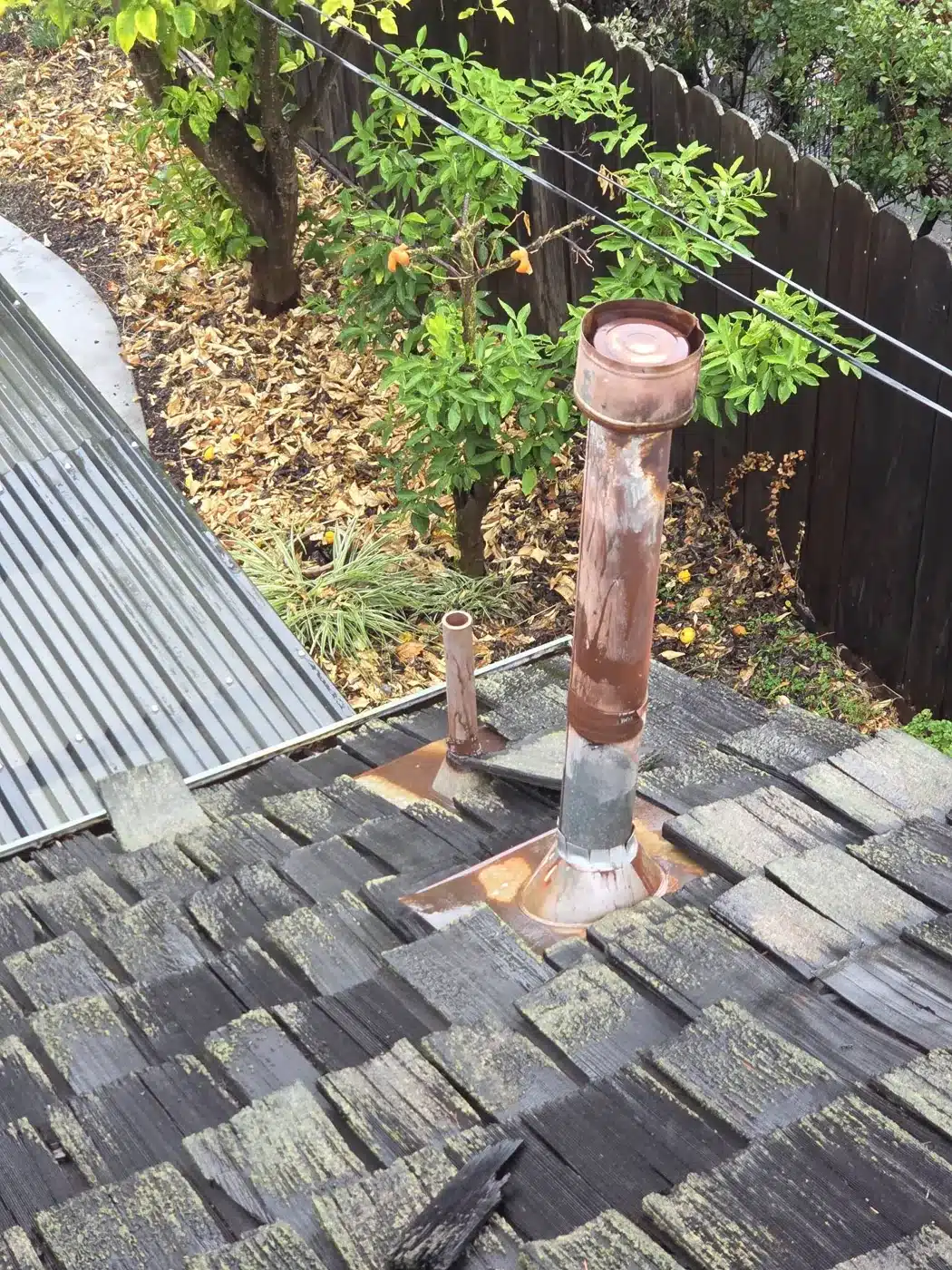 Rusted-through furnace flue penetrating an old wood shake roof in Palo Alto, CA