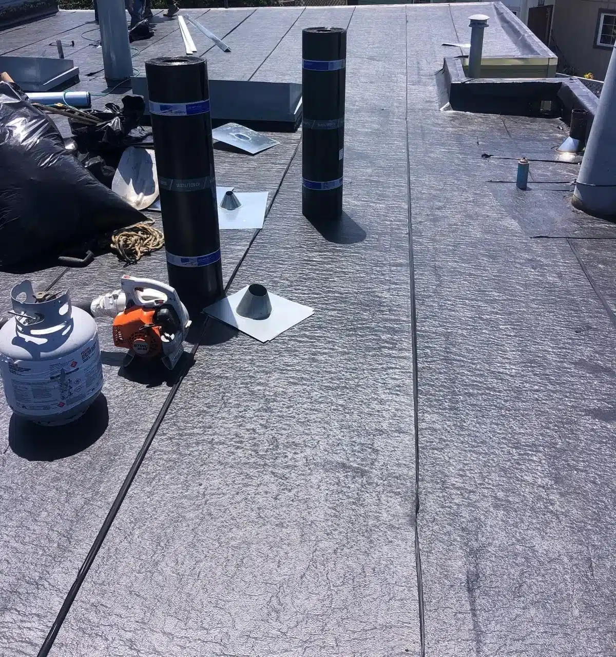 Vent stacks flashed as the new cap sheet membrane goes down on a San Francisco flat roof