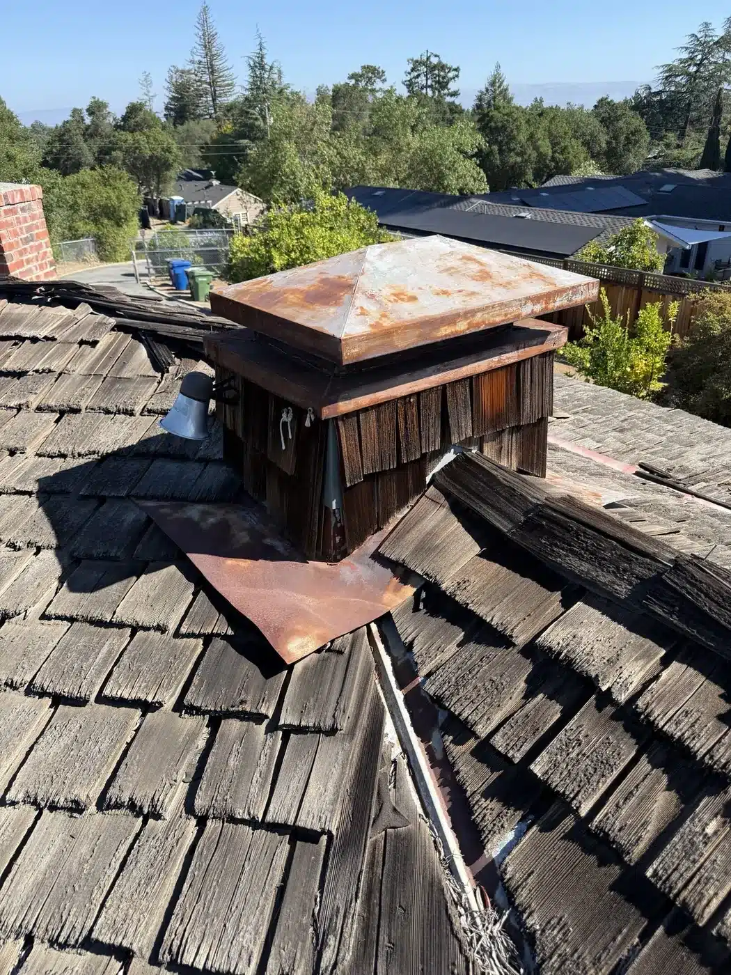 Rusted-through chimney cap on a cedar shake roof before replacement in Saratoga, CA