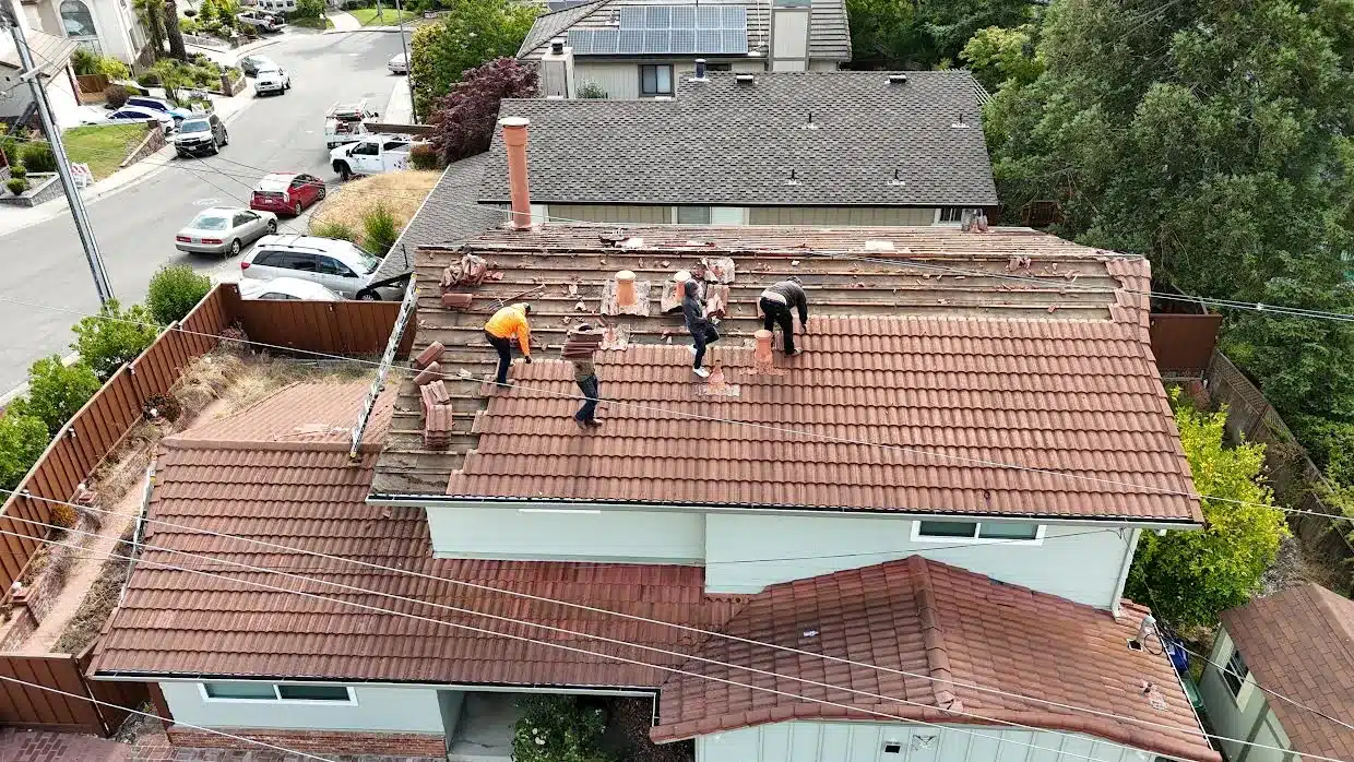 Crew removing concrete roof tiles by hand, exposing the wood battens beneath, on Proctor Road, Castro Valley CA
