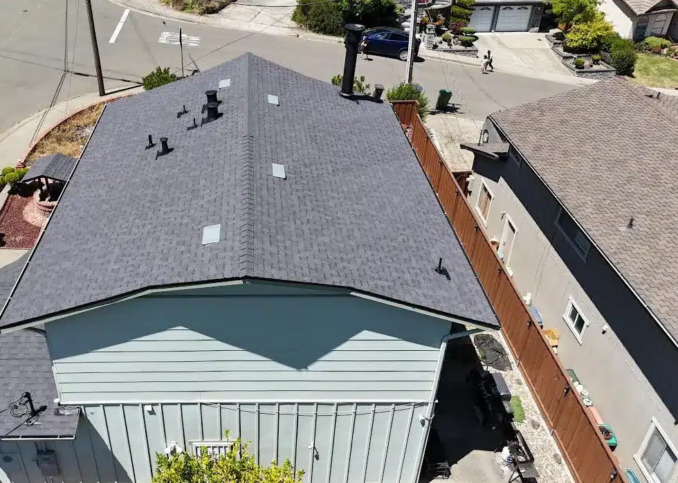 Finished architectural shingle roof seen from behind the house, with the flue pipe now black, Proctor Road, Castro Valley CA