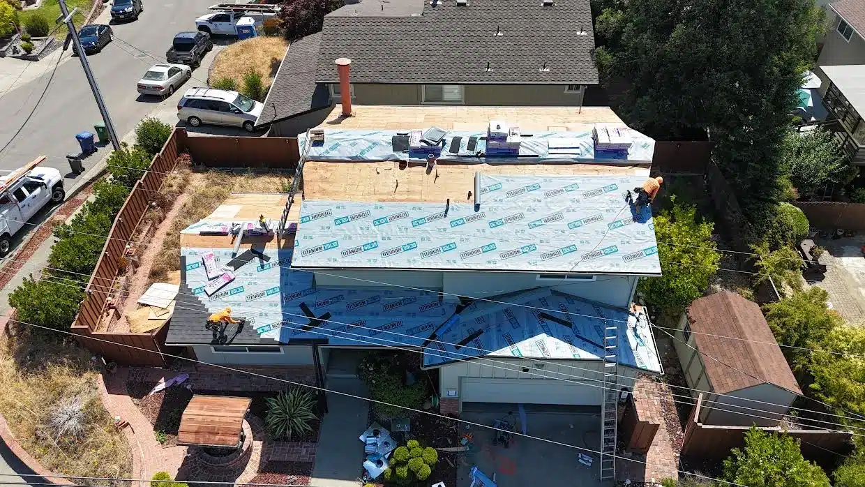 Aerial view of the house with the roof wrapped in synthetic underlayment and the first architectural shingles going on the lower roof, Proctor Road, Castro Valley CA