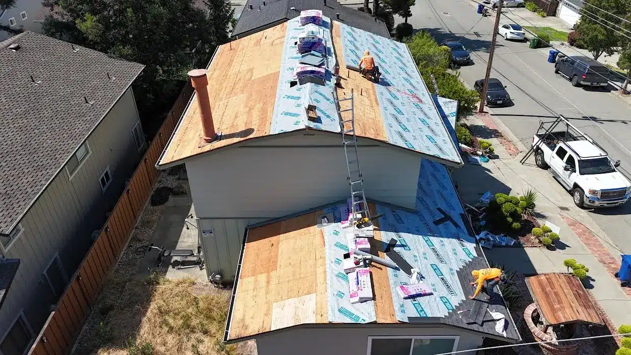 Roofers installing blue Titanium synthetic underlayment over new plywood decking with shingle bundles staged on the roof, Proctor Road, Castro Valley CA