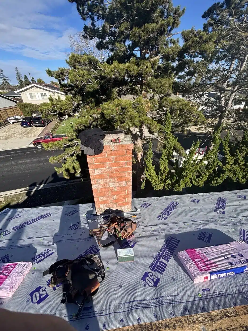 Synthetic underlayment and bundles of Owens Corning Duration COOL shingles beside the chimney during a San Jose reroof