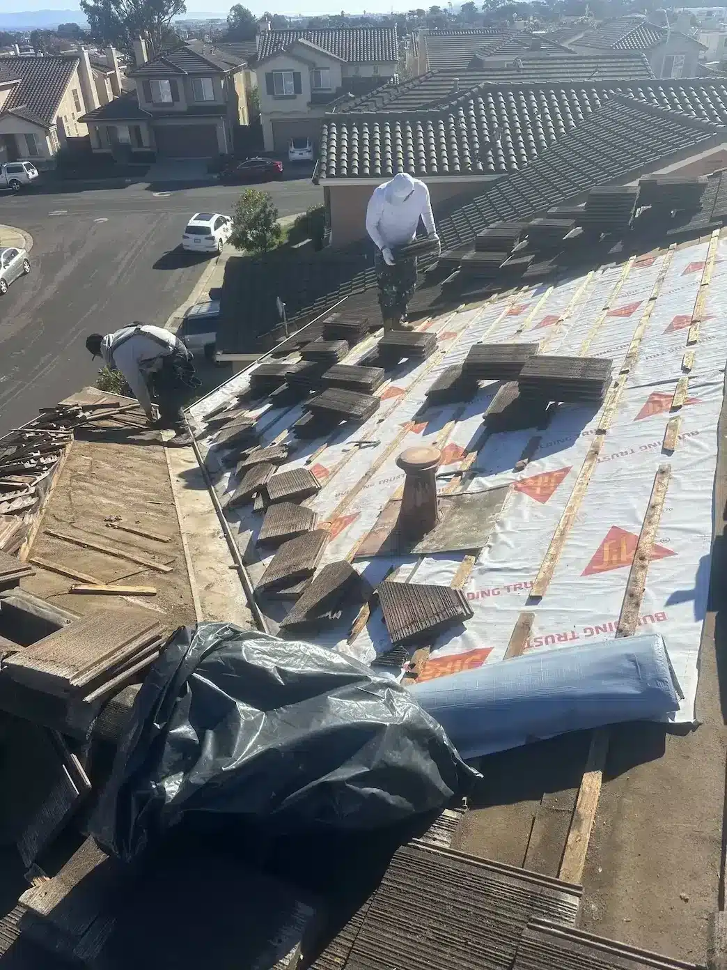Crew lifting and stacking concrete tiles over new Sika synthetic underlayment during tile roof repair in South San Francisco